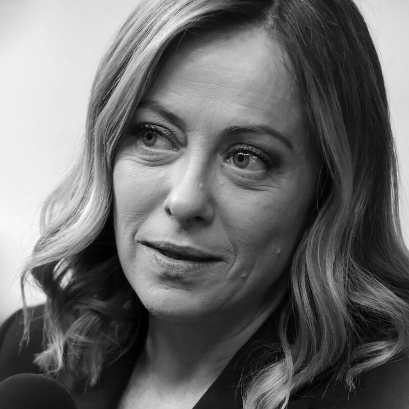 Porträt einer Frau mit welligem, schulterlangem Haar, die ernst in die Kamera schaut.