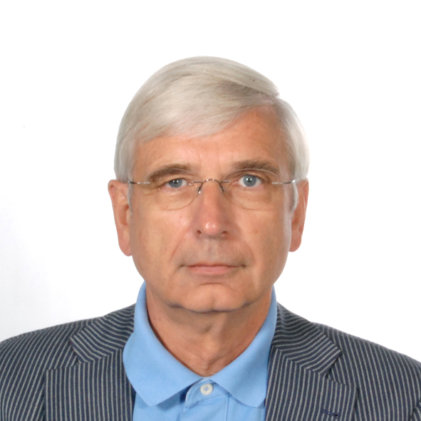 Porträt eines Mannes mit grauen Haaren, Brille und gestreiftem Blazer, vor neutralem Hintergrund.