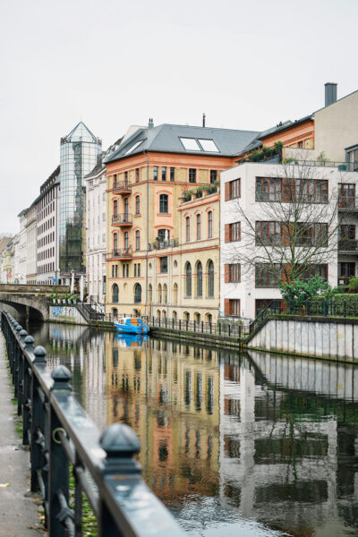 georg-baumann-depiWjIb1CA-unsplash_ - Relation Magazin Spiegelung von historischen Gebäuden am Kanal mit einem blauen Boot und einer Brücke im Vordergrund.