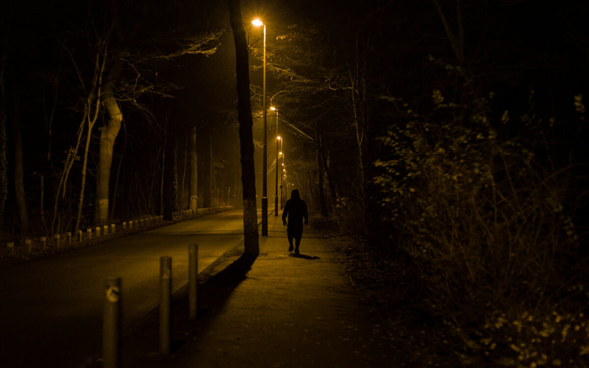 julien-V1GNTKkKhWM-unsplash_ - Relation Magazin Dunkle Straße mit einer einsamen Person, umgeben von Straßenlaternen und Bäumen, in einer nächtlichen Atmosphäre.