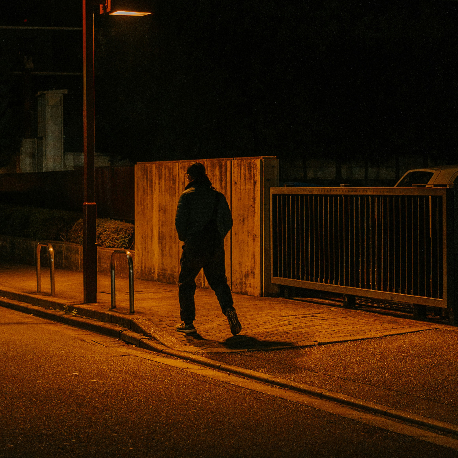Mann in dunkler Kleidung geht nachts auf einer leeren Straße, beleuchtet von einer Straßenlaterne.